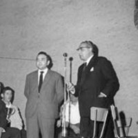 Oholtzan, Euskaltzaindiako xx mikrofono aurrean hizketan. Aldamenean zutik, Alfonso Irigoien  gai-jartzailea. Eserita, xx, Lazkao Txiki eskuan kopa duela, xx. --